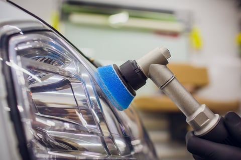 auto mechanic buffing and polishing car headlight Car detailing - man with orbital polisher in auto repair shop. Selective focus.