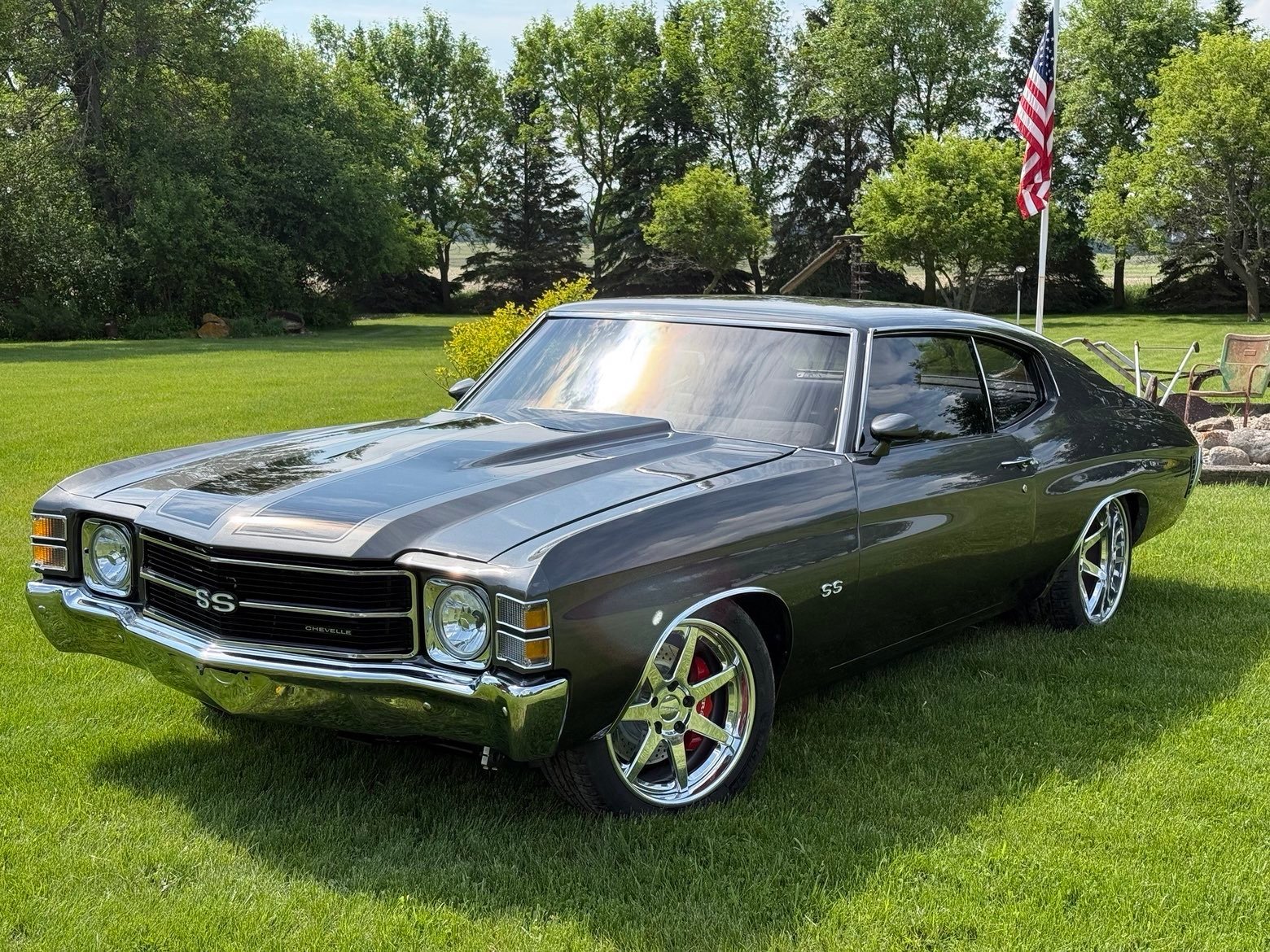 Black Chevrolet Chevelle SS muscle car displayed on grass at outdoor car show with American flag in background