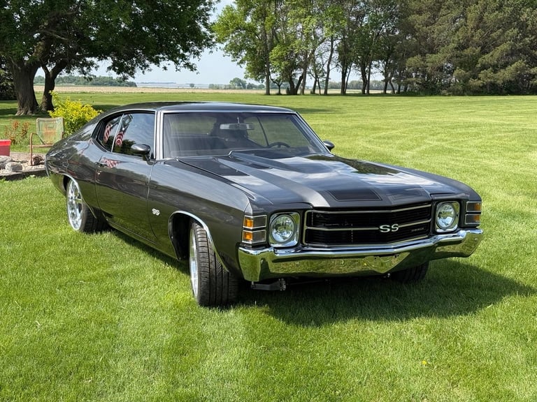 Classic black Chevrolet SS muscle car with white racing stripes parked on grass at a car show