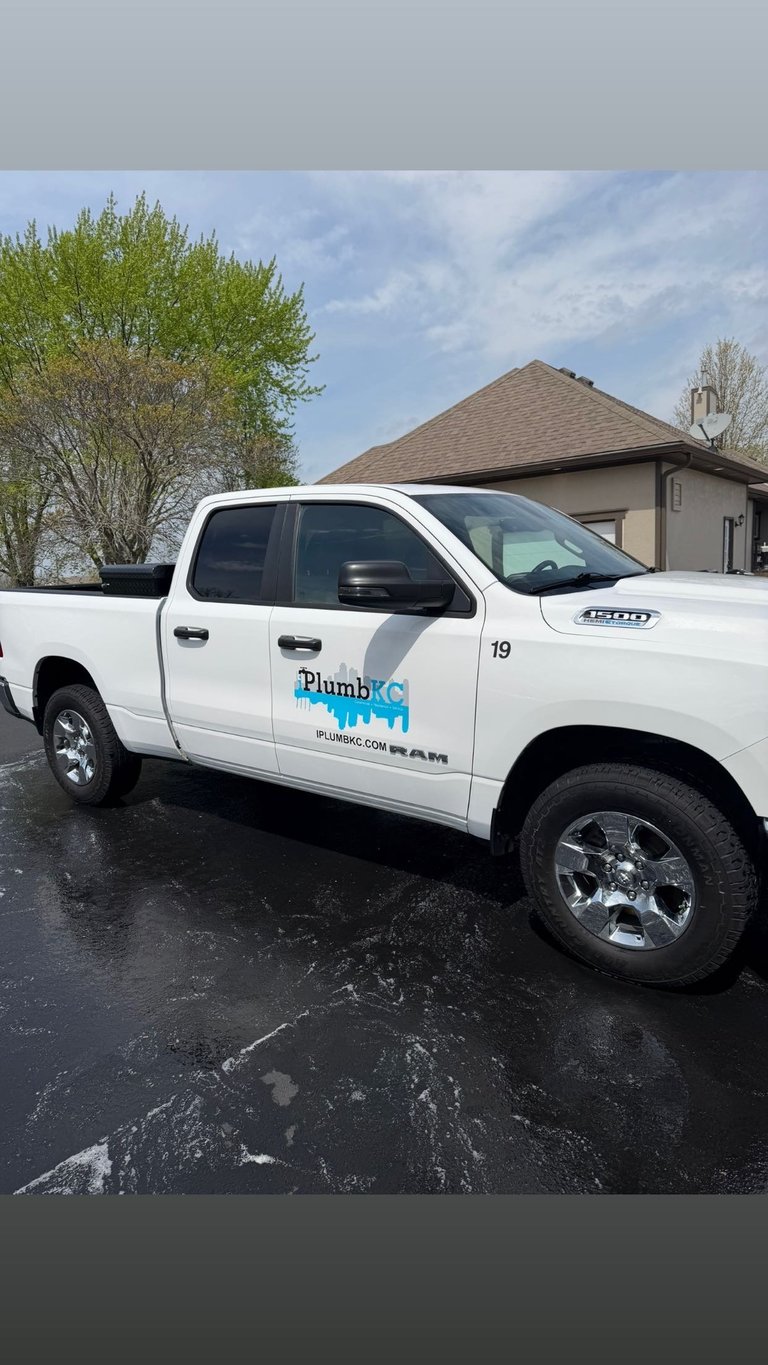 White Plumb KC service pickup truck parked in a driveway with a house and trees in the background