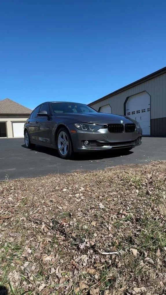 Gray BMW sedan parked in driveway with garage and blue sky in background
