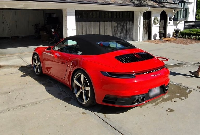 Red Porsche 911 Carrera sports car parked in driveway with black convertible top and open door