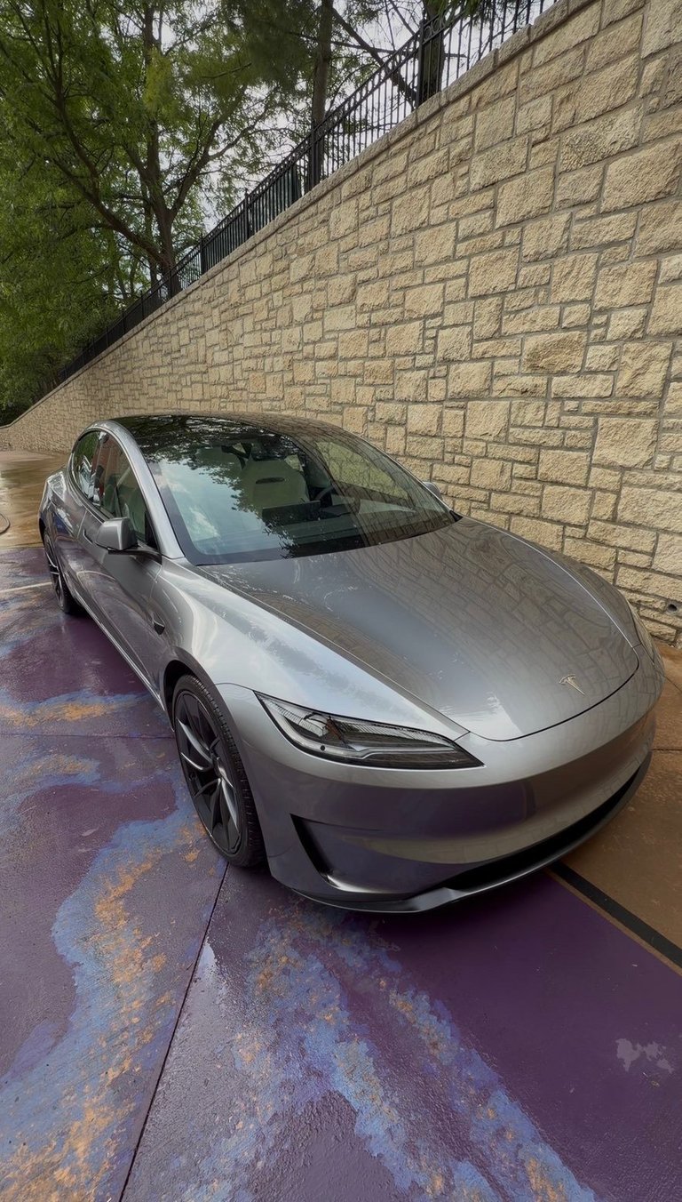 Silver Tesla Model 3 parked against a stone brick wall with metal railing above