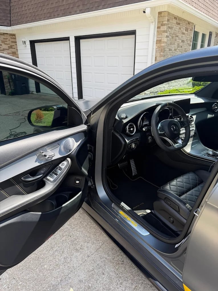 Open driver door of luxury sedan showing black leather interior and steering wheel with garage in background